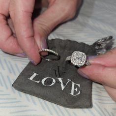 two women are holding onto their wedding rings on top of a cloth bag with the word love printed on it