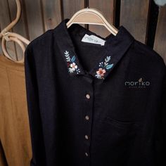 a black shirt with embroidered flowers on the front and back, hanging from a wooden hanger