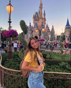 a woman standing in front of a castle at disney world holding a drink and posing for the camera