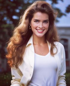 a woman with long brown hair wearing a white jacket and smiling at the camera while standing in front of a house