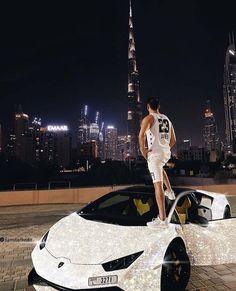 a man standing on top of a white sports car in front of a city skyline