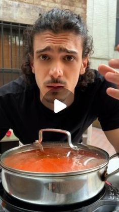 a man sitting at a table with a pot of soup in front of his face