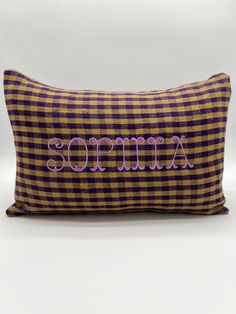 a purple and yellow plaid pillow with an embroidered name on it