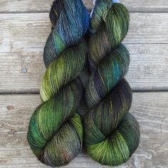 two skeins of green and blue yarn sitting on top of a wooden table