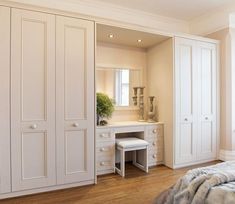 a bedroom with white furniture and wooden flooring is shown in this image, there are two doors open to reveal the dressing area