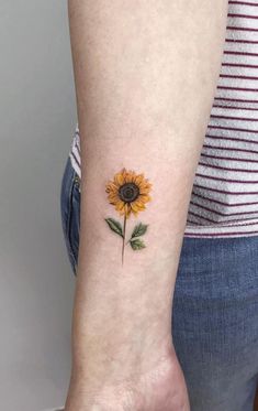 a small sunflower tattoo on the left inner arm, with green leaves and yellow petals