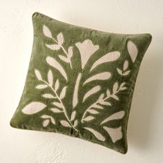 a green pillow with white flowers on the front and back, against a white wall