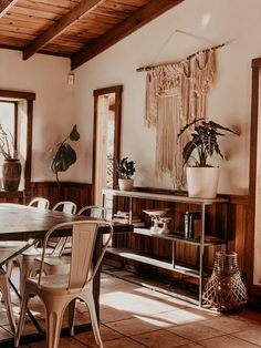 a dining room table and chairs in front of windows with potted plants on them