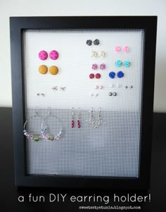 a black frame holds several pairs of earring holders in front of a white wall