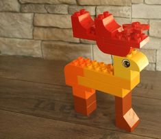 an orange and yellow toy horse made out of legos on a wooden table next to a brick wall