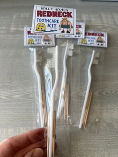 three toothbrushes in plastic bags with stickers on the top and one being held by a person's hand