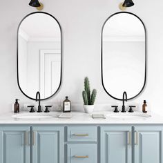 two oval mirrors are above the double sinks in this white bathroom with blue cabinetry