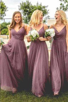 three bridesmaids in purple dresses laughing and standing on the grass with their bouquets