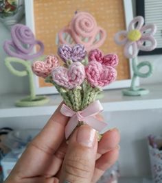 a hand holding a small crocheted bouquet of flowers in front of a frame