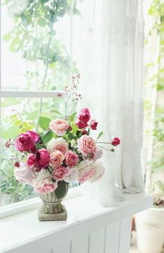 a vase filled with lots of pink and red flowers on top of a window sill