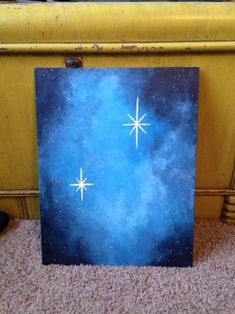 a painting is sitting on the floor in front of a yellow bench with a blue sky and stars painted on it