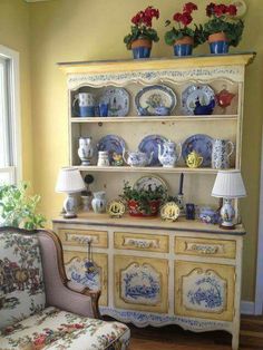 an old china cabinet with blue and white dishes on it's top, next to a chair