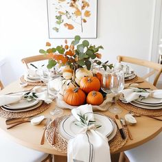 a table set for thanksgiving dinner with pumpkins and greenery on the centerpiece