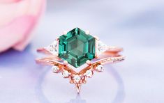 an emerald colored ring with diamond accents on the side and pink rose petals in the background