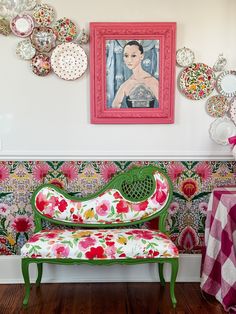 a green bench sitting in front of a wall with plates on it and a painting above it