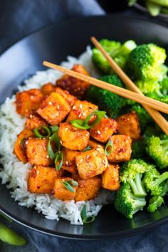 a plate with rice, broccoli and tofu on it next to chopsticks