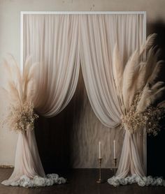 two white drapes with flowers and feathers on them in front of a wall decorated with candles