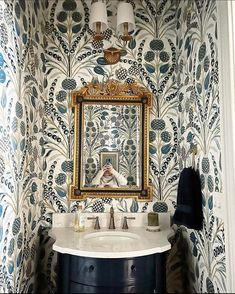 a bathroom sink with a mirror above it next to a wallpapered wall and a painting on the wall