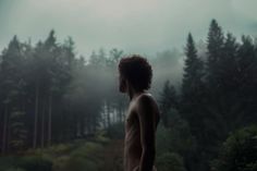 a shirtless man standing in front of trees on a foggy day with the sun behind him