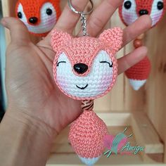 a hand holding three small crocheted keychains in the shape of foxes