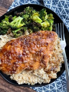 a black plate topped with chicken and rice covered in sauce next to broccoli