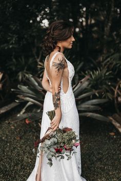 a woman in a white dress holding a bouquet and looking at the back of her dress