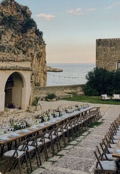 a long table set up for an outdoor dinner by the ocean