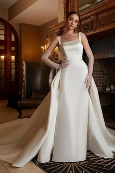 a woman in a white wedding dress standing next to a fireplace with her hands on her hips