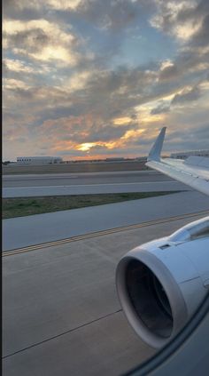 an airplane wing with the sun setting in the background and clouds over the tarmac