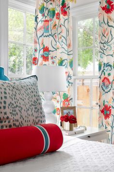 a bedroom with colorful curtains and pillows on the bed, along with a red throw pillow