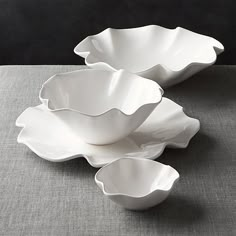 three large white bowls sitting on top of a gray tableclothed surface with one bowl in the shape of a flower