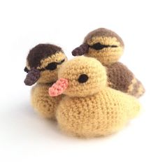 two knitted ducks sitting next to each other on a white surface, one with a pink flower in it's mouth