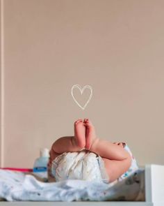 a baby laying on top of a bed next to a wall with a heart drawn on it