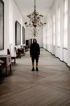 a man standing in an empty hallway with chandelier and paintings on the walls