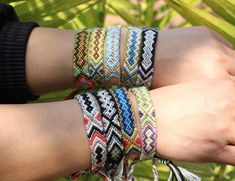 two hands wearing bracelets with tassels on each hand and palm leaves in the background