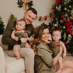 a man and woman sitting on a couch with two babies in front of a christmas tree