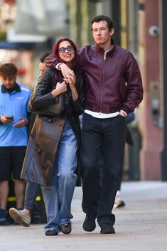 a man and woman walking down the street with their arms around each other's shoulders