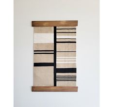 a white wall hanging with a black and beige striped rug on it's side