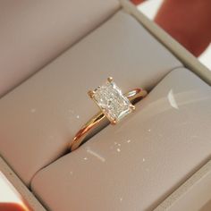 an engagement ring with a princess cut diamond set in it's gold band inside a box