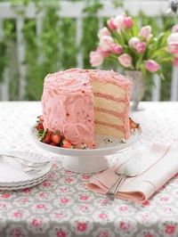 a cake with pink frosting sitting on top of a table next to plates and utensils