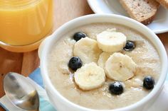 a bowl of oatmeal with bananas and blueberries next to a glass of orange juice