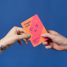 two hands holding up a pink and orange card