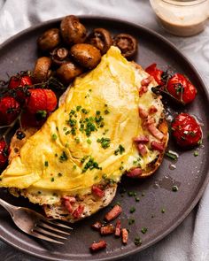 an omelet with bacon, tomatoes and mushrooms on a plate next to a fork