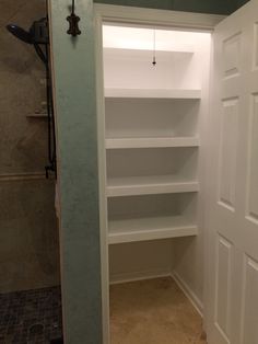 an empty walk in closet next to a shower with no curtain on the door and shelves