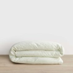 two white linen pillows stacked on top of each other in front of a white wall